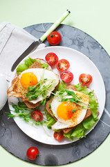 Sandwiches with fried egg, ham, tomatoes, peas sprouts and salad. Breakfast on a white plate. Top view