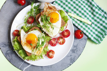 Sandwiches with fried egg, ham, tomatoes, peas sprouts and salad. Breakfast on a white plate. Top view