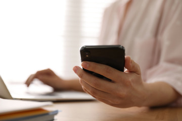 Woman with smartphone and laptop at table indoors, closeup