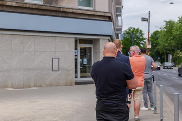 Fototapeta na wymiar Selected focus view, Group of European men with wearing face mask queue and wait for get in a bank on sidewalk during social distancing and quarantine regulations for COVID-19 virus.