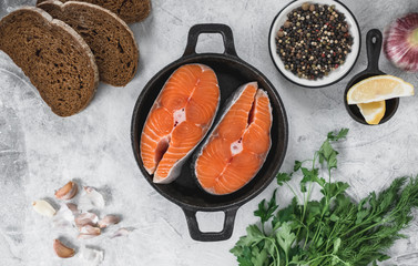 Fresh steaks of red salmon fish with spices, herbs and lemon in a black pan.