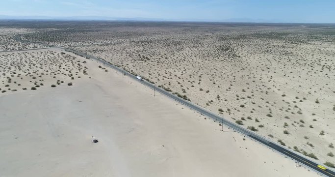 Tracking shot highlights road traversing desert and sandy environment