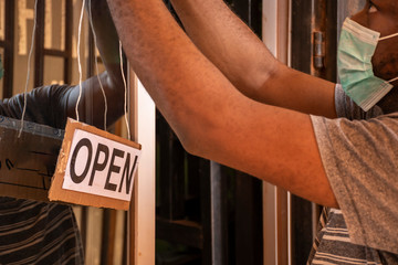 local african business owner putting up a open sign in front of his store