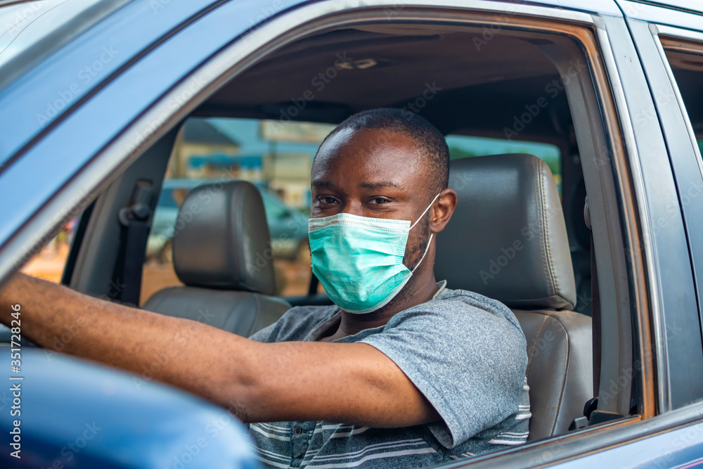 Wall mural young african man driving a car wearing a face mask