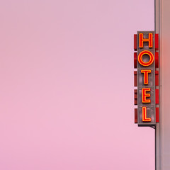 Neon hotel sign on the building corner with pink sunset sky at background.