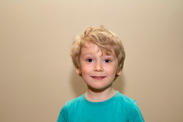 little boy with blond hair on a gray background looks joyfully and openly at the camera.