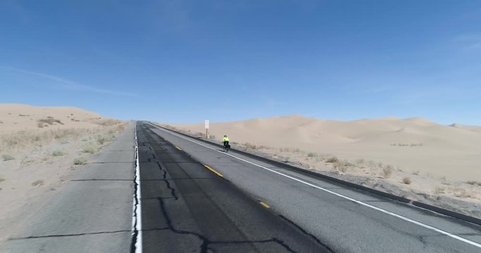 Close pass over road shows amazing perspective of cyclist riding up hill through North Algodones dunes