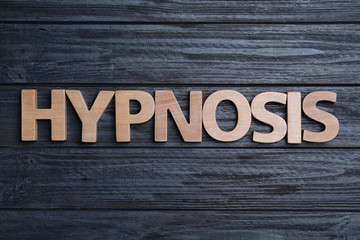 Word HYPNOTHERAPY made with wooden letters on black background, flat lay