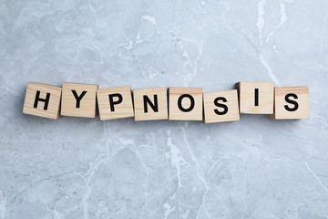 Wooden blocks with word HYPNOSIS on light grey marble background, flat lay