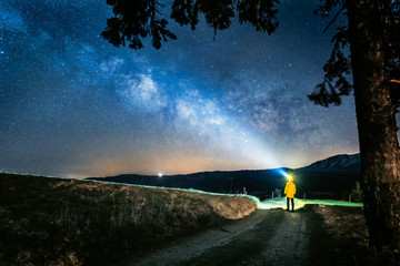 A man in yellow jacket with a headlamp staring at the Milky Way galaxy at dark night © PiotrKaluza