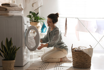 Young woman taking laundry out of washing machine at home