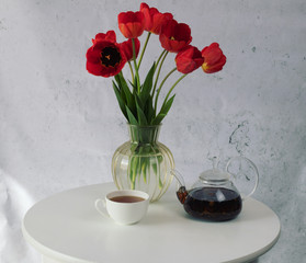 Breakfast. Tea, teapot and red tulips on wooden white round table.