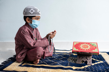A little Asian Muslim boy is sitting and praying.