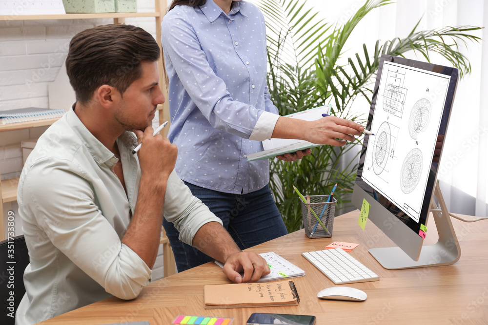 Poster colleagues working with technical drawing on computer in office