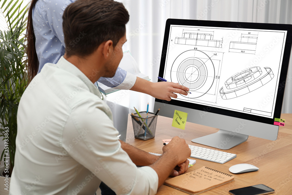 Poster colleagues working with technical drawing on computer in office