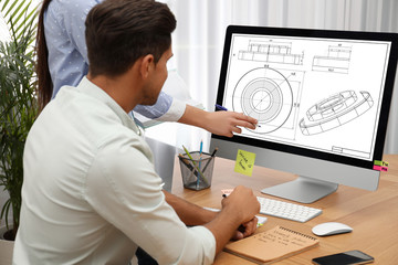 Colleagues working with technical drawing on computer in office