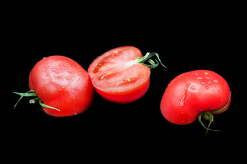 halves of ripe fresh organic tomato in dew drops isolated on a black background