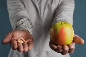 The doctor holds a pill and an apple in his hands. The concept of choosing between artificial drugs or vitamins and natural products