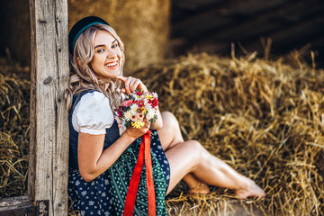 Cute blonde in dirndl, traditional festival dress with bouquet of field flowers sitting on the...
