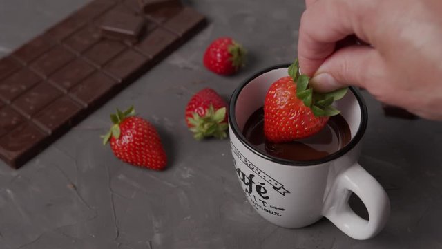 Dipping strawberry in melted dark hot chocolate. Chocolate covered strawberry cooking process