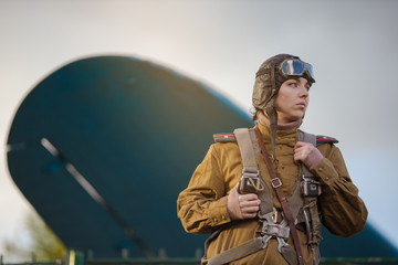 A young female pilot in uniform of Soviet Army pilots during the World War II. Military shirt with shoulder straps of a major, parachute, flight helmet and goggles. © Kozlik_mozlik