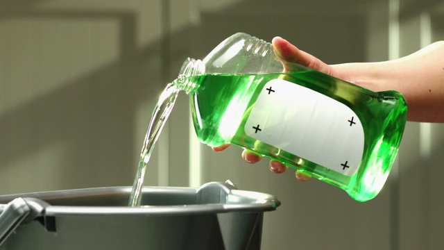 Cleaning agent is poured into bucket from transparent bottle with replaceable label place holder
