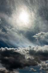 Fototapeta na wymiar dramatic stormy sky with a blurred sun disk and heavy cumulus clouds against a dense cloud cover. artwork picture for fantasy, abstract or moody design or decoration