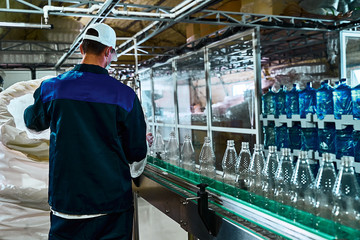 Pure drinking water plant. Work conveyor in the enterprise. A worker places liter bottles on a...