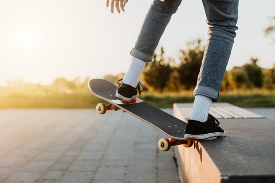 Junge Skaterin mit Jeand skatet lässig mit dem Skateboard in seiner Freizeit im Park bei Sonnenschein und grüner Landschaft im Hintergrund