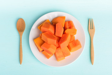 Slices of ripe papaya fruit on plate with fork and spoon on pastel color background, Tropical fruit
