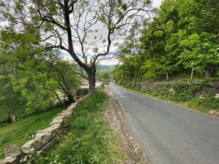 Fototapeta na wymiar A beautiful country lane, leading to the bottom of Shibden Valley, with dry stone walling and an asphalt road, late spring, in Shibden Valley, Halifax, Yorkshire, England