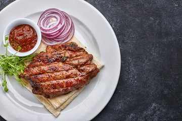 Grilled meat steak with onions, sauce and microgreen, on pita bread, on a white plate, against a dark background. space for text. top view