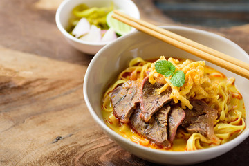 Northern Thai food (Khao Soi), spicy curry noodles soup with coconut milk and beef in a bowl and chopsticks