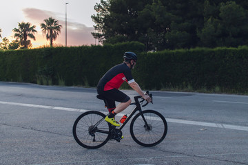Obraz premium Cyclist ride, dressed up with red and black cloths on country roads on a evening in Spain.