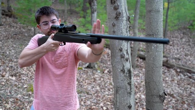 Young hipster man aims and fires a pellet rifle in a forest.