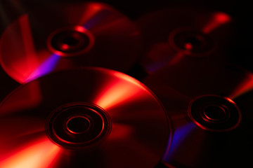 Close up of CDs and DVDs. Abstract illustration, illuminated in red, with dark shadows. Selective focus with blurred background.