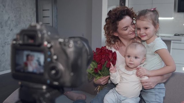 Woman has two daughters. Family is posing at home. Woman holds bouquet of tulips.