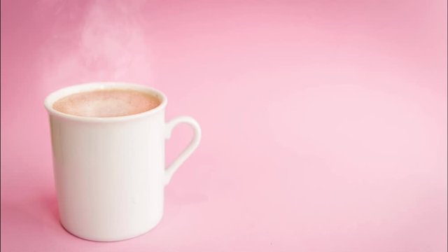 
White colored cup with hot cappuccino coffee coming out of smoke (steam) on a light pink background. Blur image for use in backgrounds.