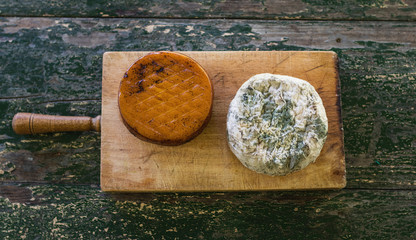 Top view of two cheeses on a wooden board on a rustic table. Smoked cheese and moldy blue cheese.