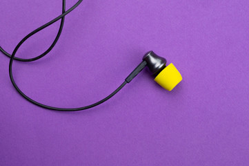 Earphone with yellow ear cushion on a purple background. in-ear headphones. modern style. audio equipment