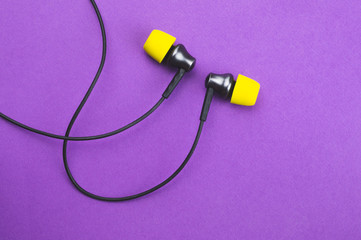 Earphones with yellow ear cushions on a purple background. in-ear headphones. modern style. audio equipment