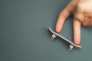 Small skateboard on color background. hand on tiny skate. fingers playing with fingerboard. home...