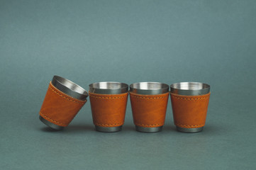 Metallic shot glasses in a row. one glass is falling. travel shot glass for alcohol with leather casing over the stainless steel