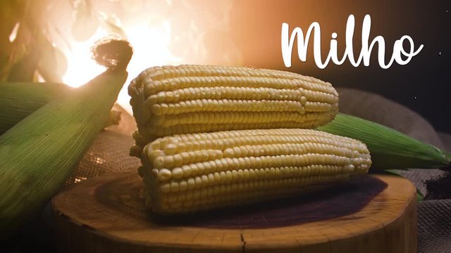 Three corn on a wooden board. Beside it appears written in Portuguese: Milho