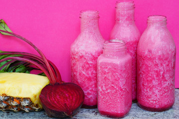 Glass bottles filled with colorful fresh homemade beet and pineapple smoothies