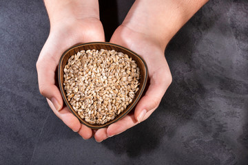 Female hands holding bowl with pearl barley - Hordeum vulgare