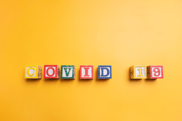 flat lay copy space of colorful wooden alphabet blocks spelt as COVID-19, representing coronavirus disease transmission worldwide pandemic infectious virus in Wuhan china, isolated yellow background