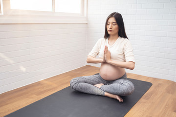 Fototapeta na wymiar Beautiful asian pregnant woman meditating yoga pose sitting on yoga mat training practicing yoga breathing, healthy and fit motherhood feeling happy and strong, pregnancy expecting future new born