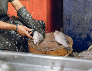 Hombre moreno trabajando quitando escamas en un pescado fresco