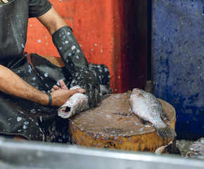 Hombre moreno trabajando quitando escamas en un pescado fresco